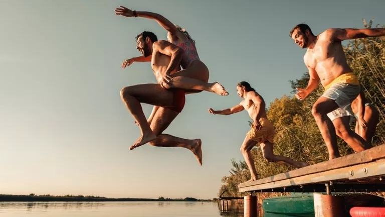 Summer-time-fun-group-of-friends-socializing-on-a-lake.-Jumping-off-a-dock.webp